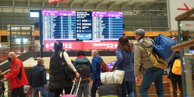 Travellers stand in front of an information board at BER Airport in Berlin, Germany, Saturday, Dec. 18, 2021. Germany’s incoming transport minister is advising people against traveling over Christmas as the country tries to stem a wave of coronavirus infections. (Joerg Carstensen/dpa via AP)