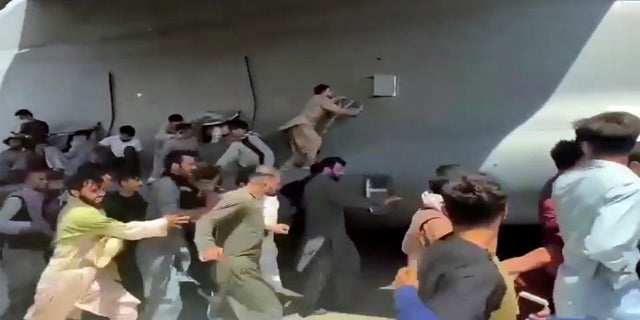 Hundreds of people run alongside a U.S. Air Force C-17 transport plane, some climbing on the plane, as it moves down a runway of the international airport, in Kabul, Afghanistan, on Monday.