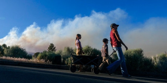Residents walk by as smoke rises from the Sheep Fire burning in Wrightwood, Calif., Sunday, June 12, 2022.
