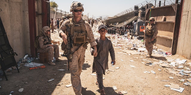 A U.S. Marine with the Special Purpose Marine Air-Ground Task Force-Crisis Response-Central Command (SPMAGTF-CR-CC) escorts a kid to his family during an evacuation at Hamid Karzai International Airport, Kabul, Afghanistan, Aug. 24. U.S. service members and coalition forces are assisting the Department of State with a non-combatant evacuation operation (NEO) in Afghanistan.
