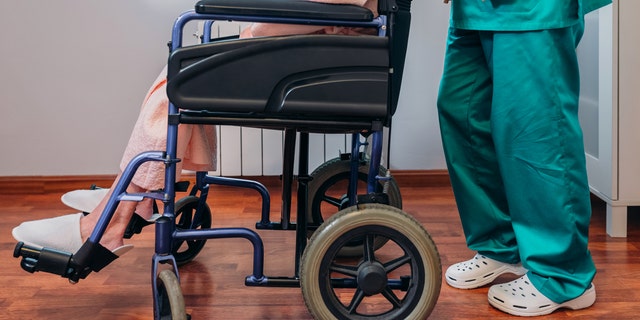 Female doctor carrying elderly female patient in a wheelchair